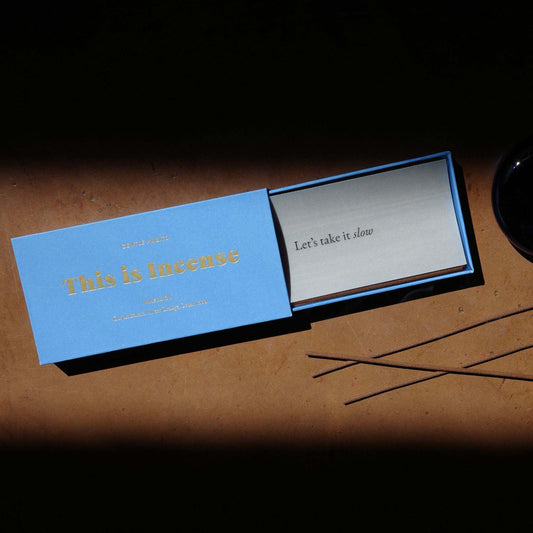 Open blue Gentle Habits incense box revealing silver card and brown sticks on warm surface by 9to5 Studios