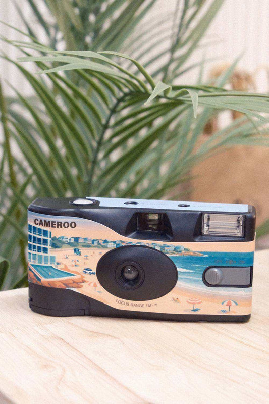 Disposable film camera with a Sydney beach illustration, blue and peach artwork, and a black lens; One Camera, 27 Frames