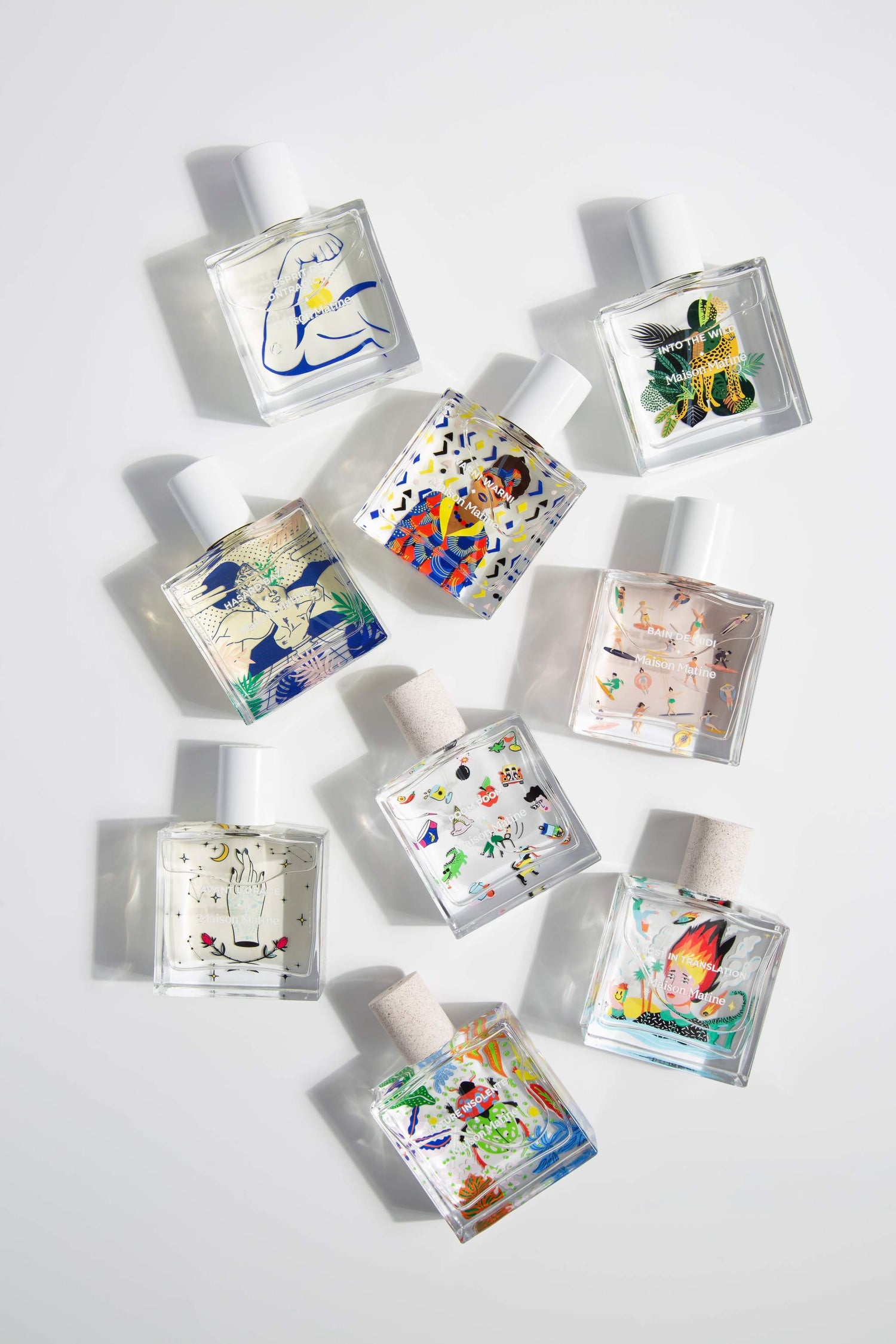 MAISON MATINE INTO THE WILD perfume collection flat-lay with illustrated glass bottles featuring artistic designs like blue arm, green jaguar, and celestial hand