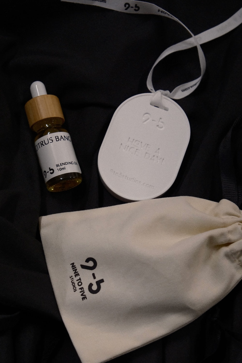 9to5 Studios car diffuser set with citrus banana oil, white oval freshener, cotton pouch, and wooden cap dropper on black fabric
