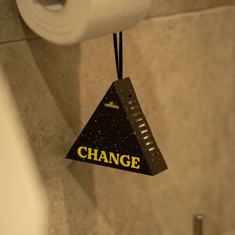 Black speckled triangular fragrance sachet with gold foil CHANGE lettering hanging in bathroom