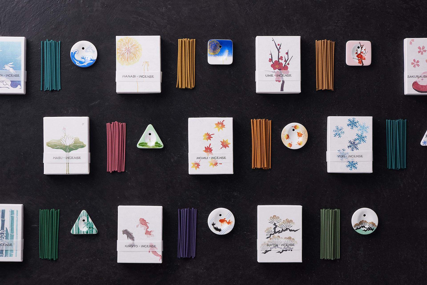 KOUSAIDO incense collection flat lay with Japanese botanical motif boxes, ceramic holders, and colored sticks on black surface