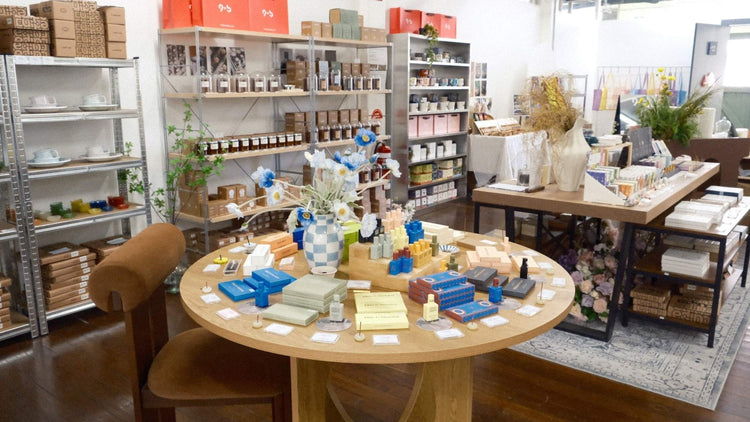 9to5 Studios curated home decor collection featuring blue checkered ceramic vases, matte storage boxes with gold foil, and wooden display table in modern retail space