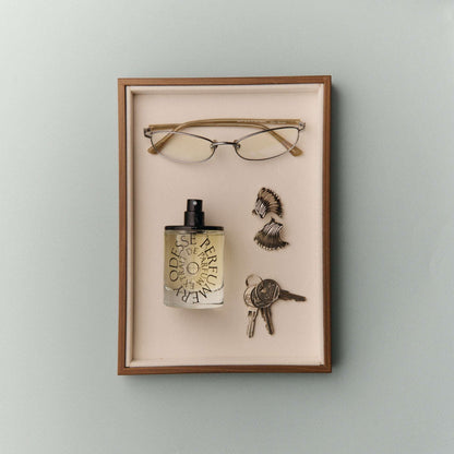 Odesse Extrait De Parfum displayed in velvet shadow box with gold-rimmed glasses, seashell earrings, and vintage keys