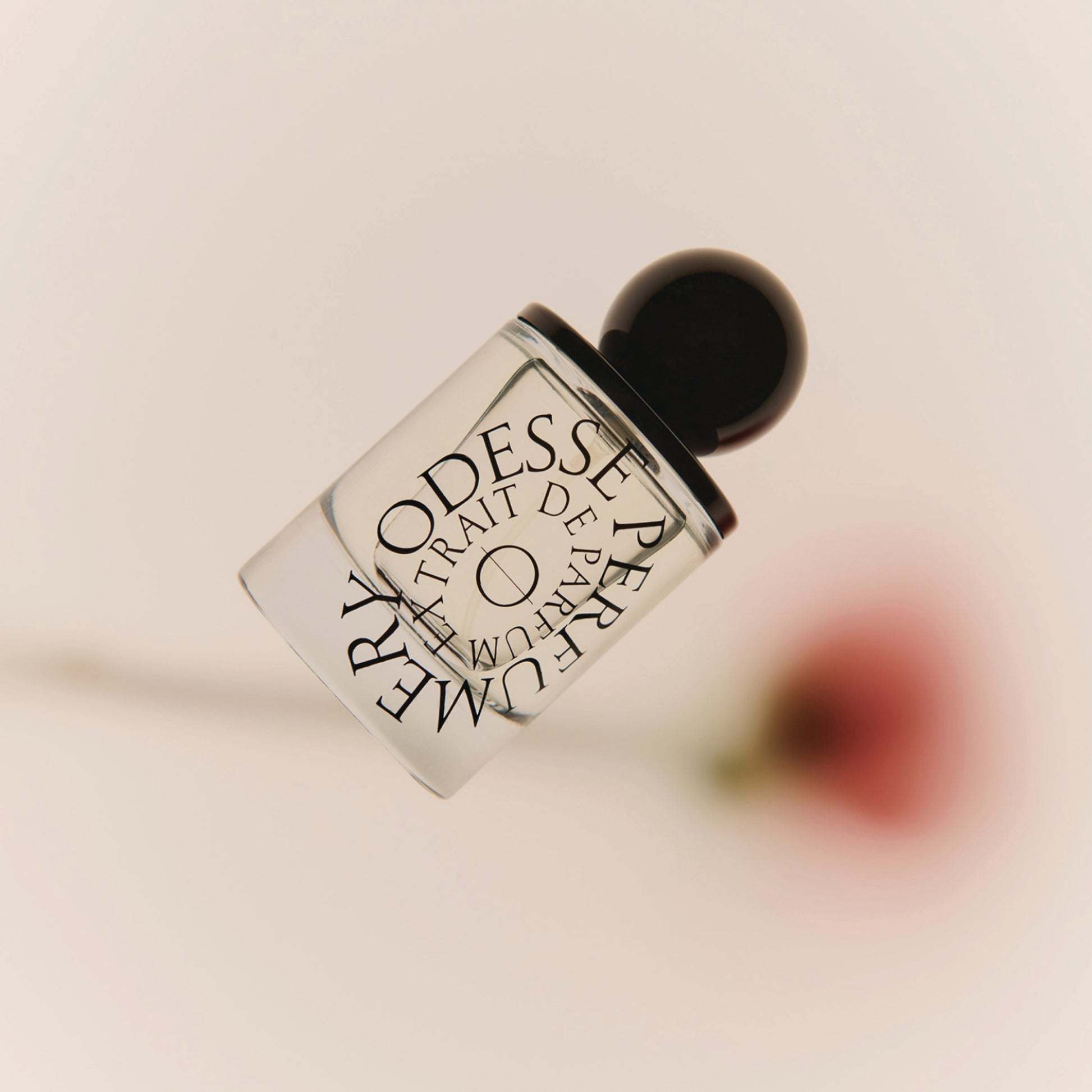 Tilted Odesse Rose Wood bottle against pink background with rose petal by 9to5 Studios