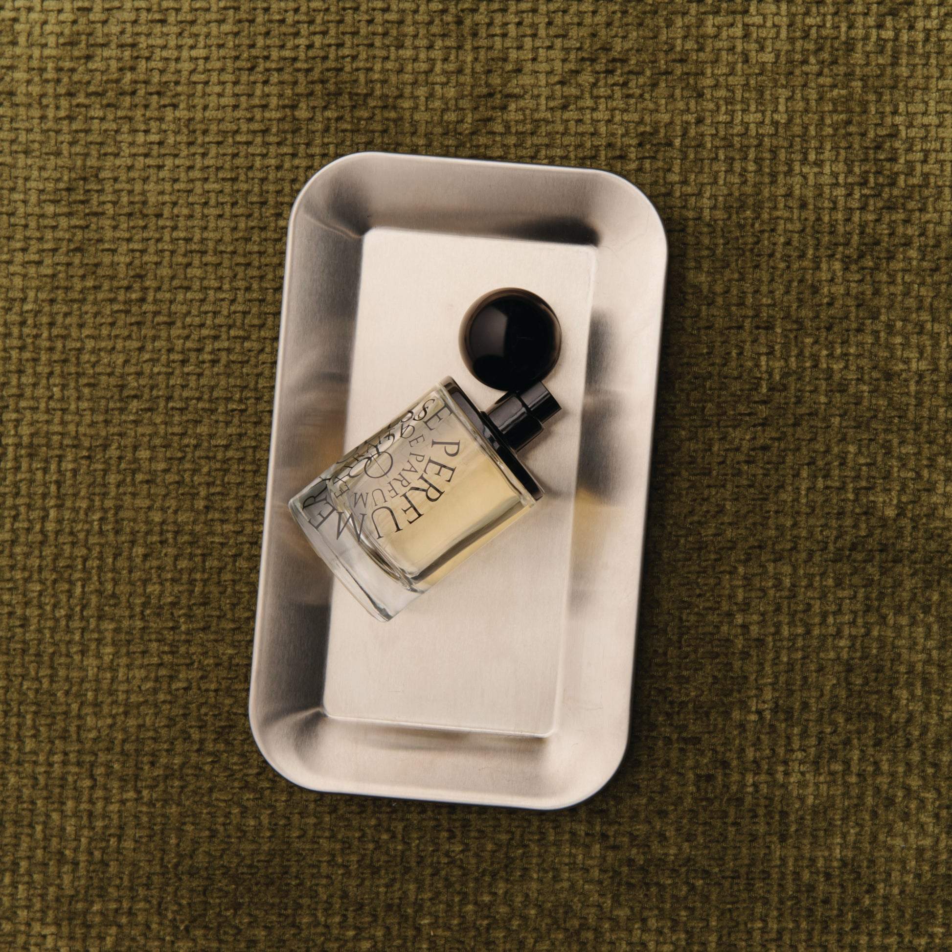 Odesse The Valley perfume bottle on brushed silver tray with olive fabric background at 9to5 Studios