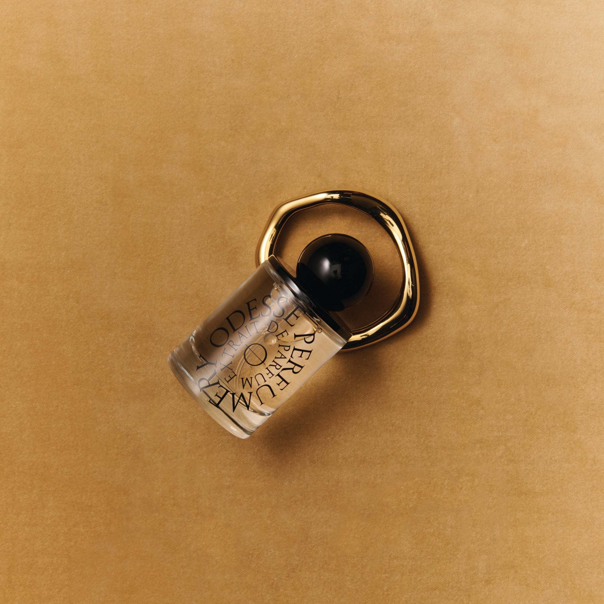 Odesse perfume bottle with gold ring accessory on tan background at 9to5 Studios