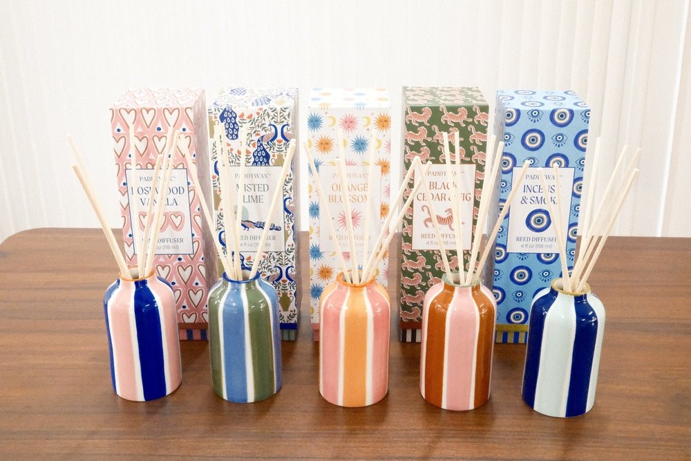 Five Paddywax reed diffusers in colorful striped ceramic vessels with coordinating retail boxes