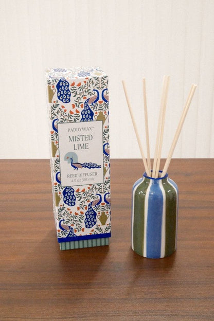 Paddywax Misted Lime reed diffuser with olive green and royal blue striped ceramic vessel on wooden surface