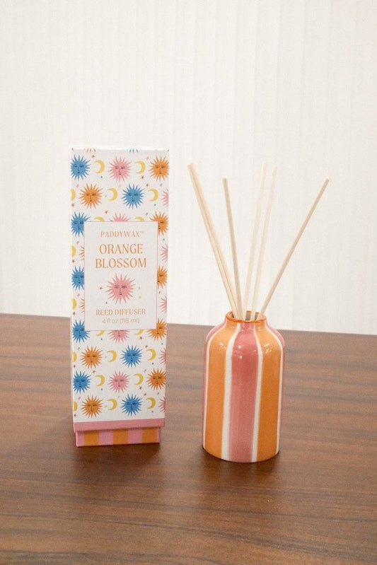 Paddywax Orange Blossom Reed Diffuser side view coral peach white striped bottle on wood table with illustrated box