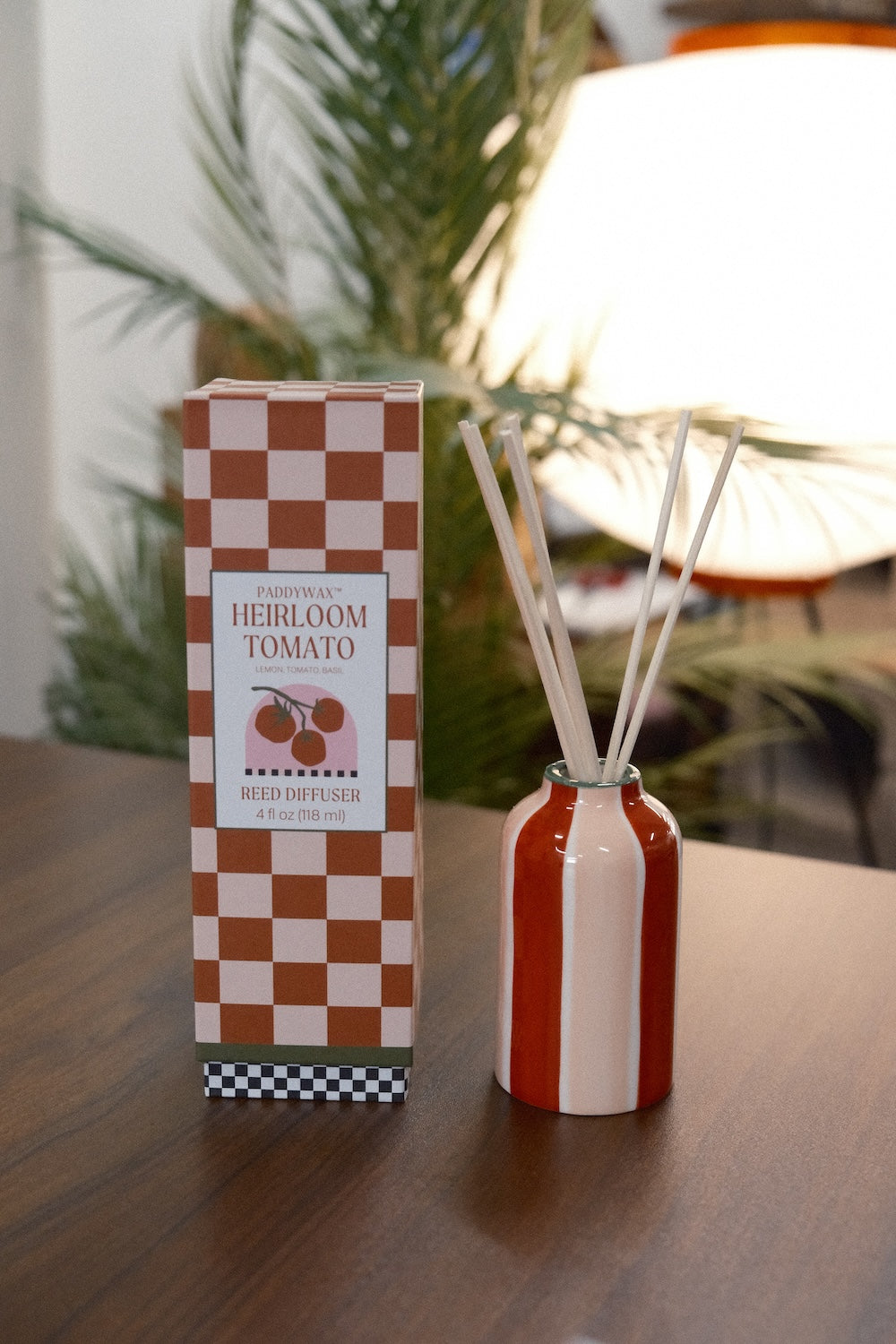 Paddywax A Dopo Tomato diffuser with orange cream stripes beside box on wood table with palm plant