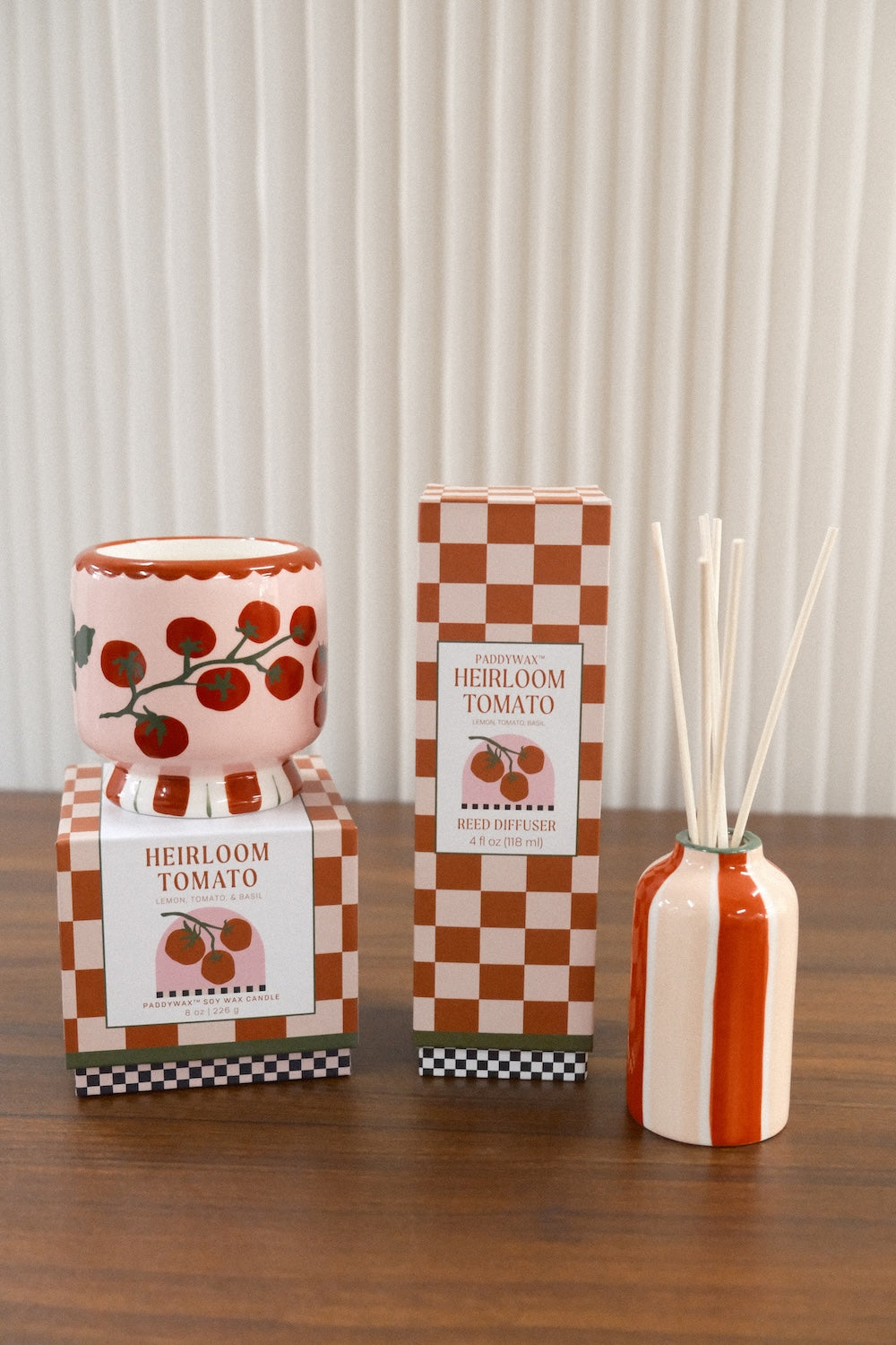 Paddywax Heirloom Tomato Reed Diffuser next to matching pink tomato candle on wooden surface