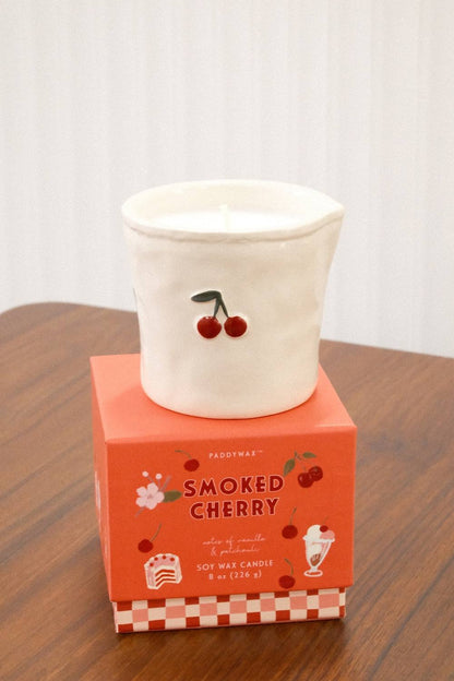 Paddywax Bistro Smoked Cherry candle on orange-pink checkered box displayed on wooden table
