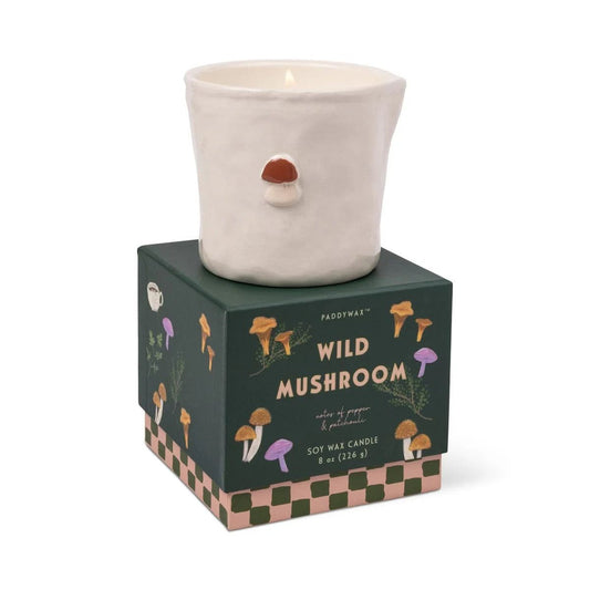 Paddywax Wild Mushroom soy wax candle in textured off-white ceramic with embossed mushroom detail, lit on dark green illustrated box