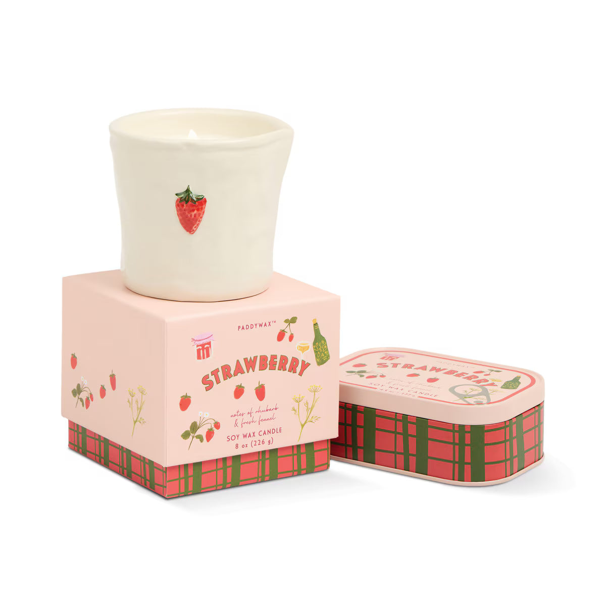 Lit Paddywax Bistro Strawberry candle in ceramic vessel with open plaid metal tin beside box