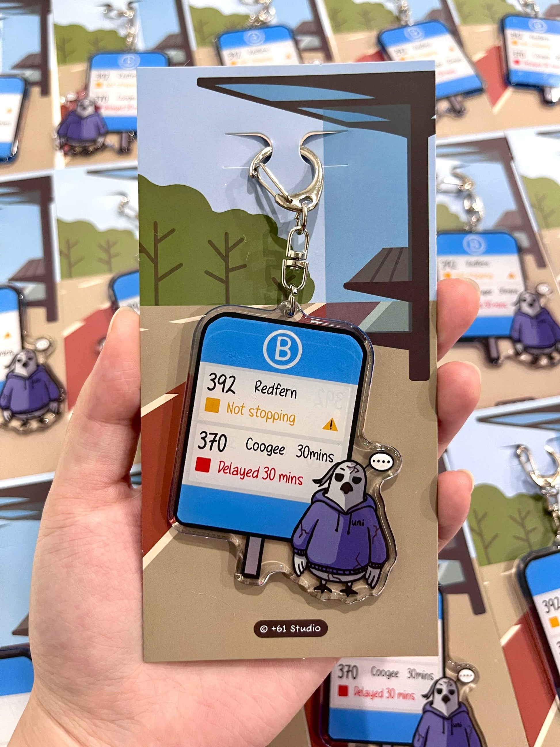 +61 Studio Bus keychain featuring a deadpan cockatoo frozen after bus delay, double-sided acrylic design with metal clasp