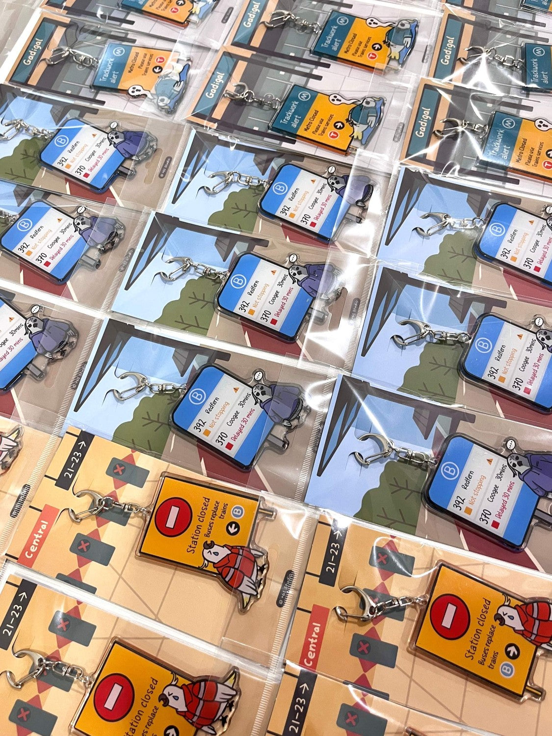 9to5 Studios bulk display of packaged acrylic keychains including Not Stopping and Station Closed variants