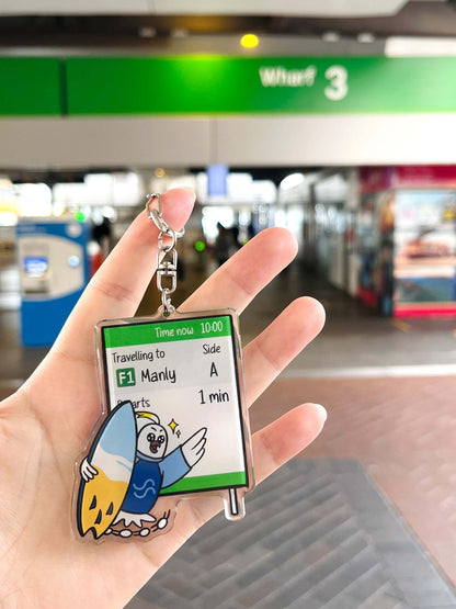 9to5 Studios Sydney harbour travel souvenir keychain held at ferry terminal, clear acrylic with cockatoo and surfboard detail