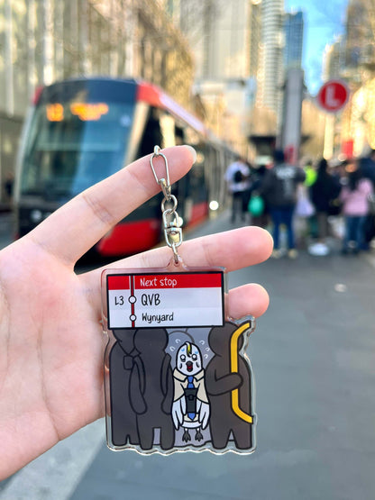 9to5 Studios Manly ferry keychain lifestyle shot held against blurred Sydney light rail train background