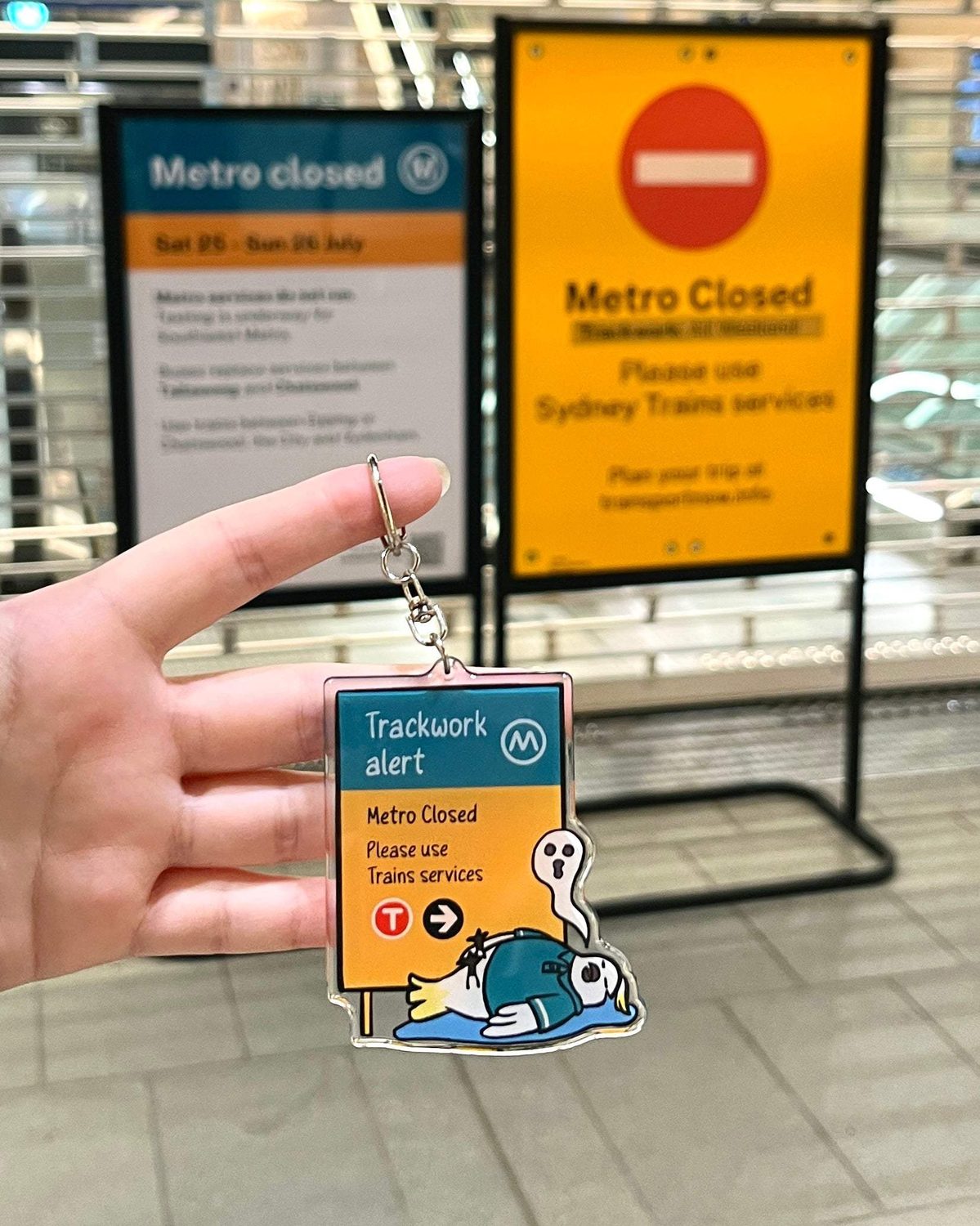 +61 Studio Metro Trackwork Alert Keychain by 9to5 Studios held at station with clear acrylic teal orange sign