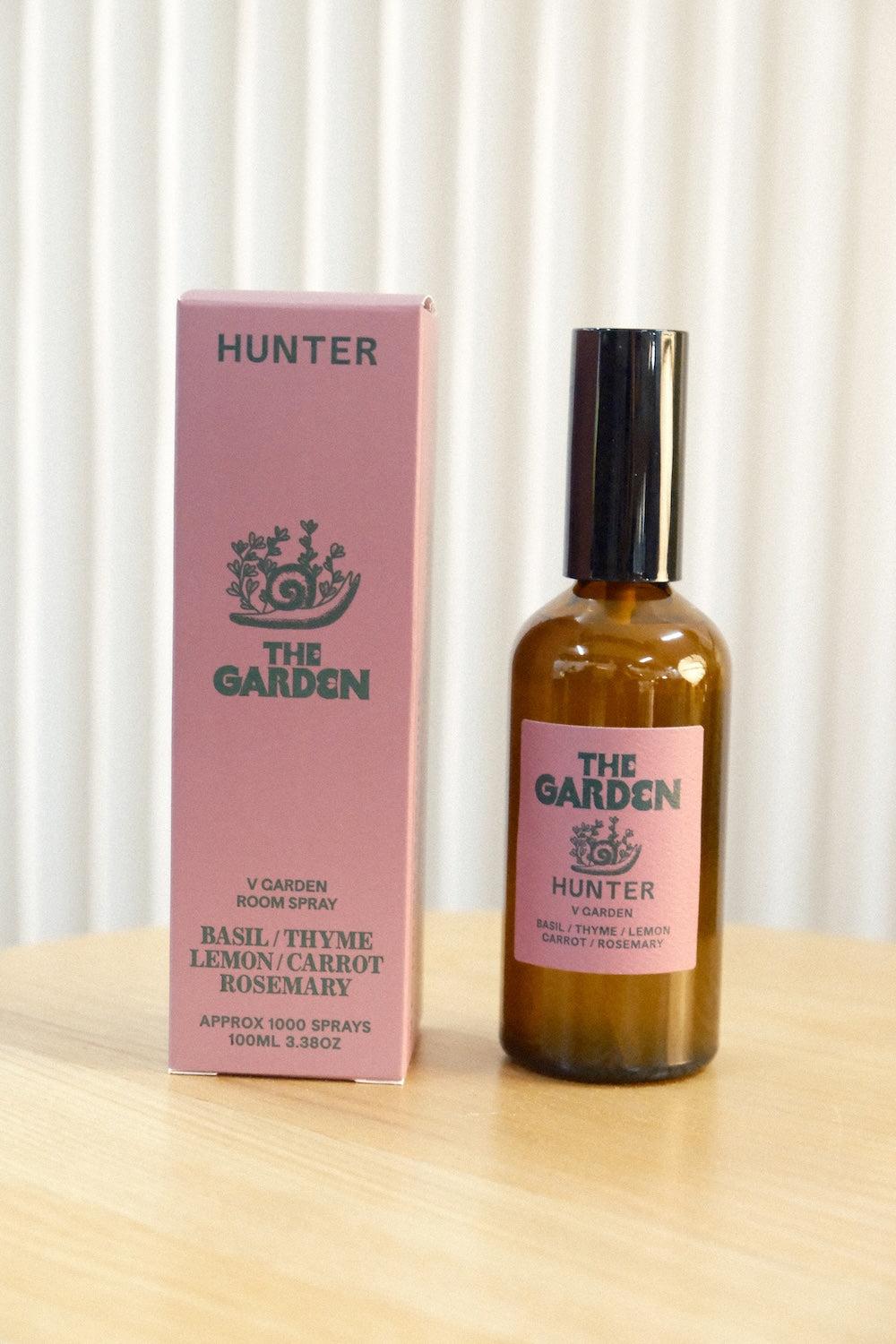Pink packaging box for The Garden room spray next to amber glass bottle