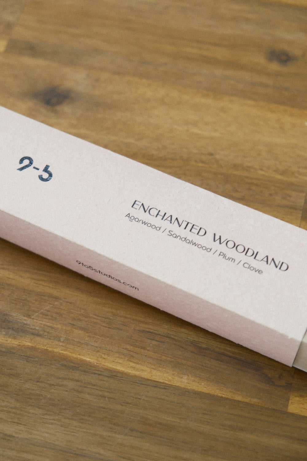 Single pink Enchanted Woodland incense box lying diagonally on brown wood surface