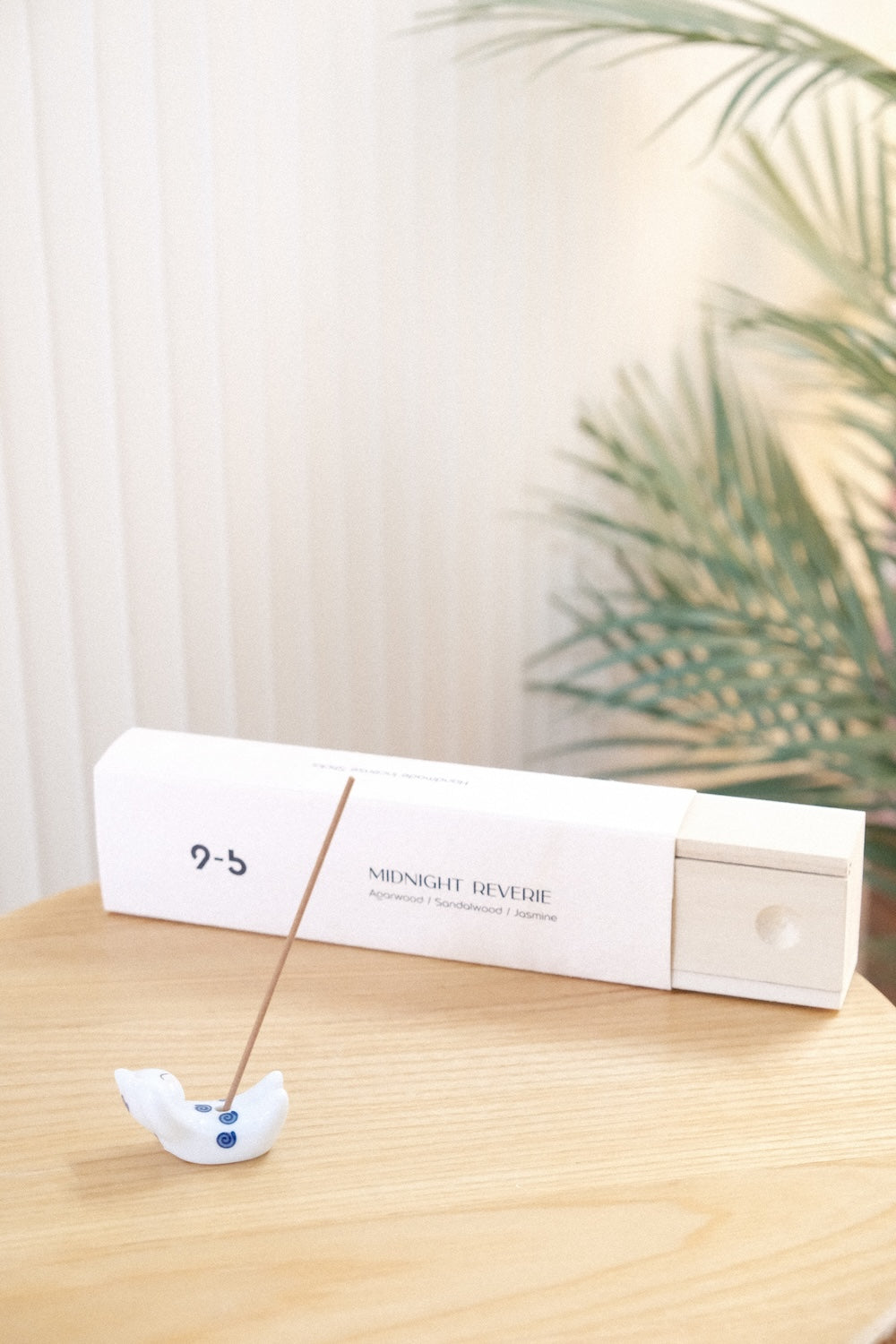 Brown incense stick in white ceramic animal holder next to open Midnight Reverie incense box with extended wood drawer