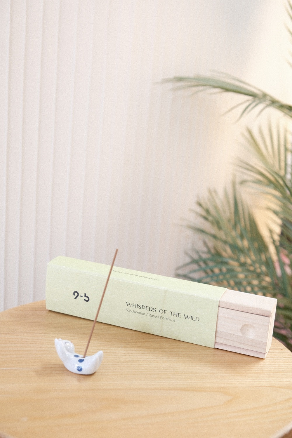 Sage green Whispers of the Wild incense box next to lit stick in ceramic holder
