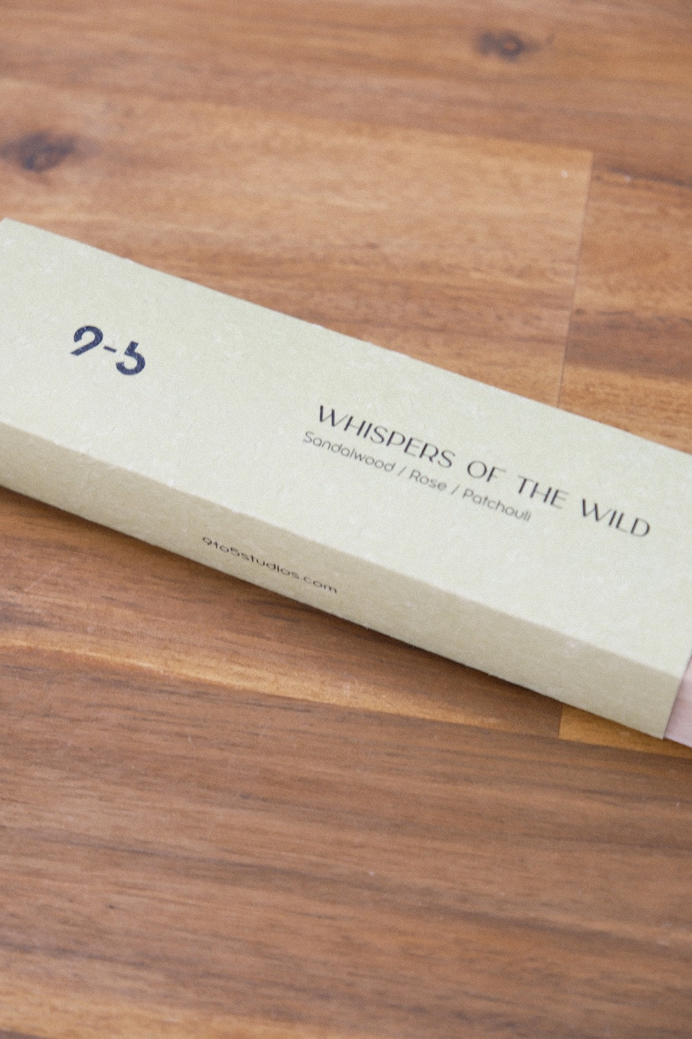 Top down view of textured pale green Whispers of the Wild incense box on dark wood