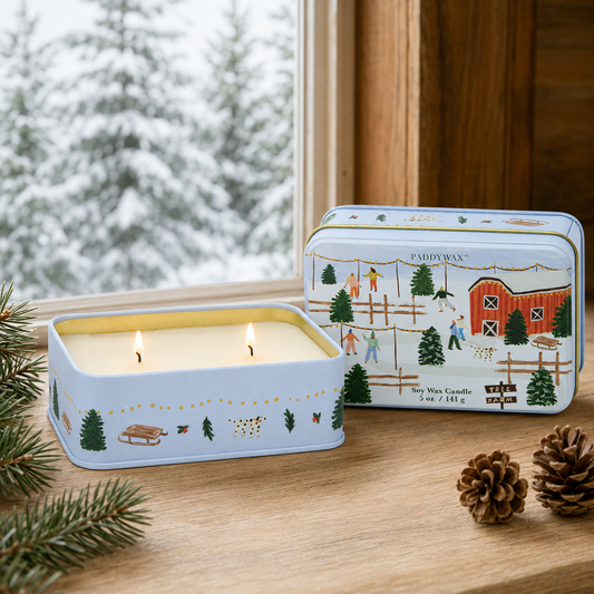 9to5 Studios lit two-wick soy wax candle in blue matte tin on wooden windowsill with snowy forest view
