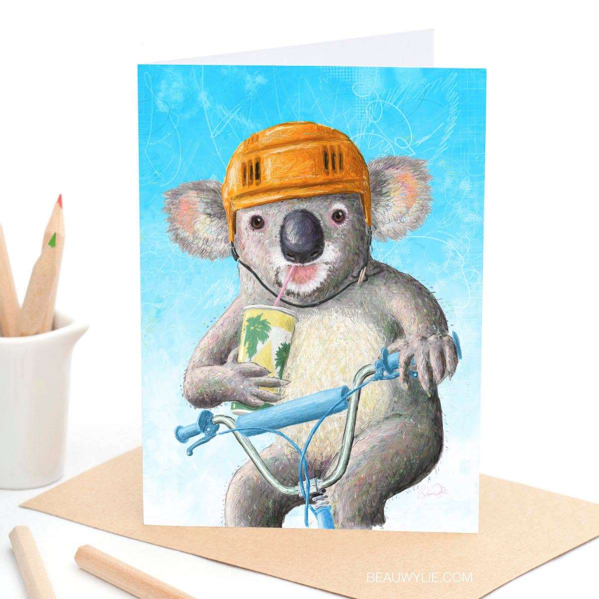 BMX Bandit greeting card by Beau Wylie for 9to5 Studios featuring grey koala on blue BMX with orange helmet and banana milkshake on recycled white cardstock