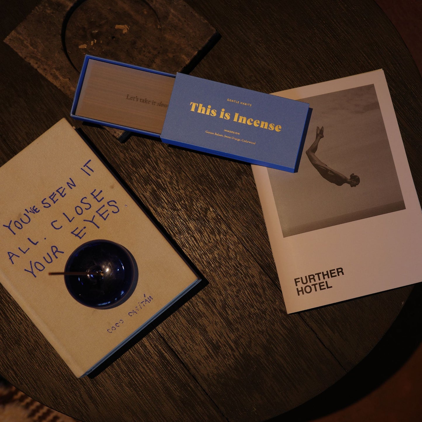 Mindful flat-lay of open blue incense box, notebook, and cobalt holder on dark wood table by 9to5 Studios