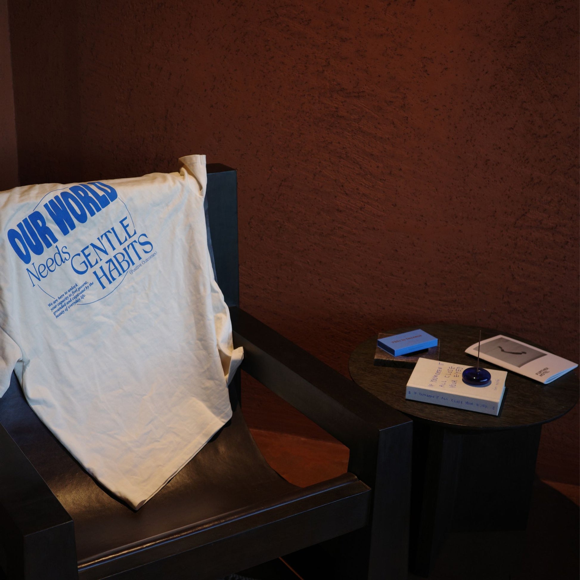 Moody interior with blue incense box, lit stick, book, and 'OUR WORLD Needs GENTLE HABITS' t-shirt by 9to5 Studios