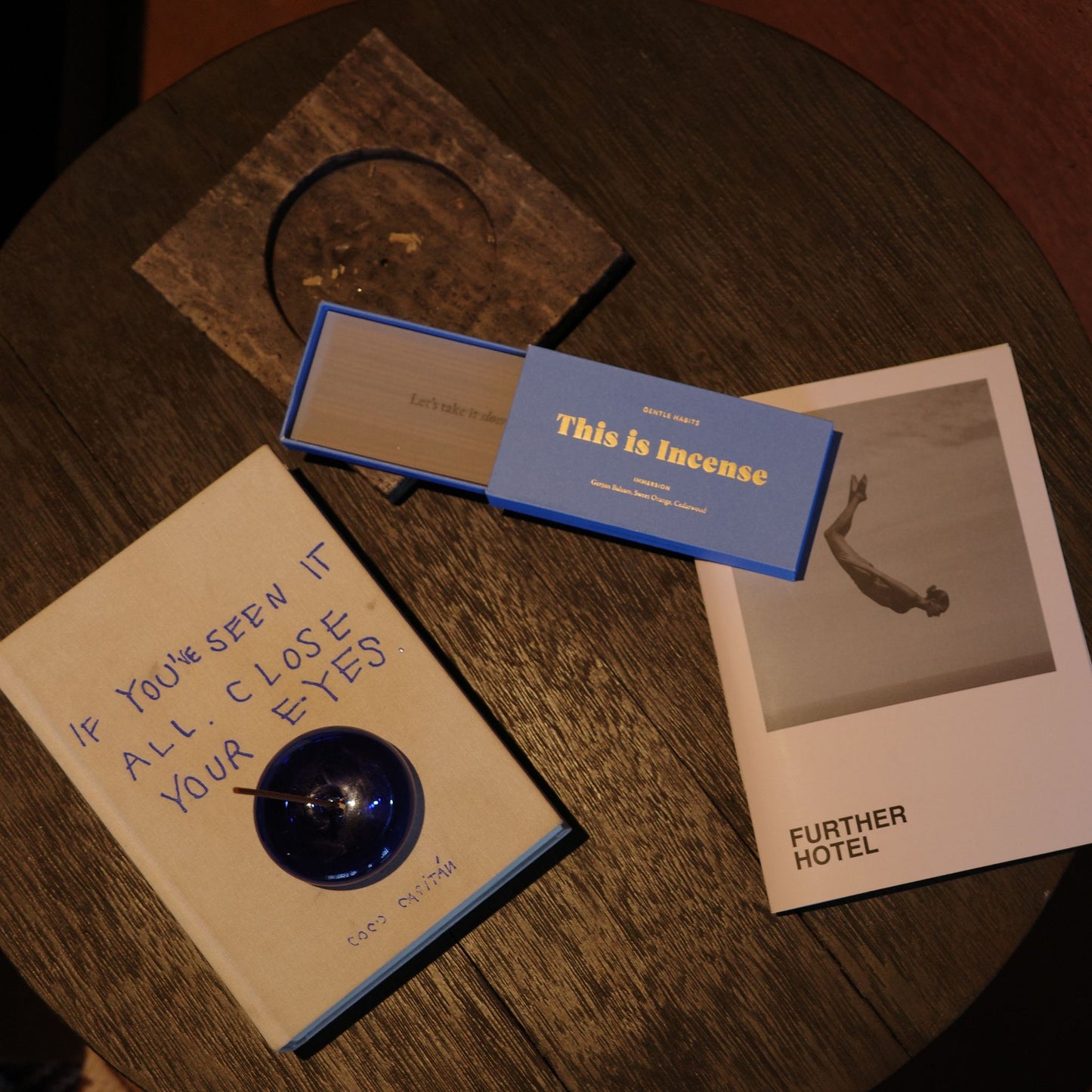 Top-down view of blue incense box on dark wood table with book and photo card by 9to5 Studios