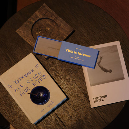 Top-down view of blue incense box on dark wood table with book and photo card by 9to5 Studios