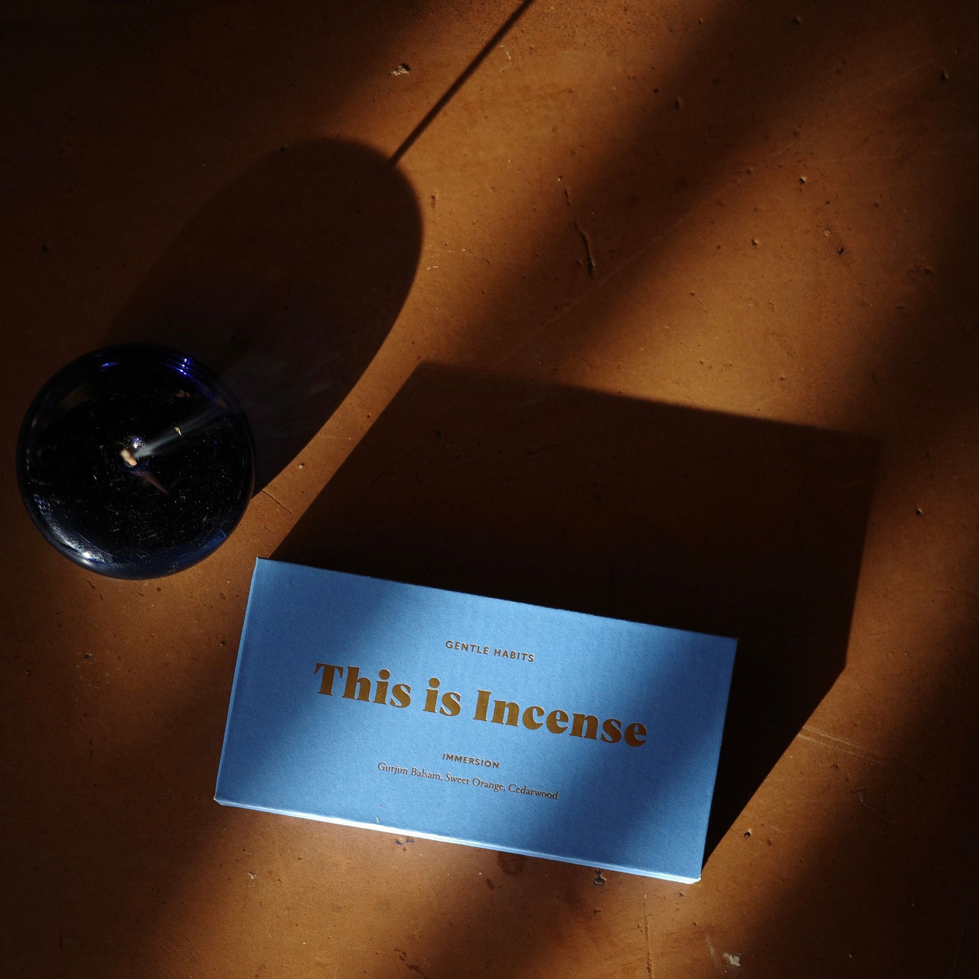 Overhead flat-lay of blue textured incense box with empty cobalt glass holder on terracotta floor by 9to5 Studios