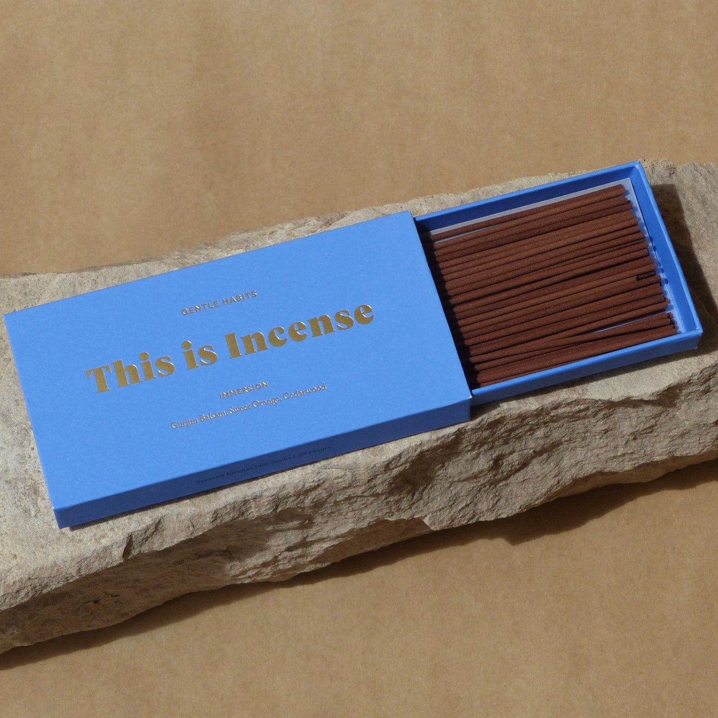 Open blue matchbox-style incense container on rough stone slab showing aligned brown sticks by 9to5 Studios