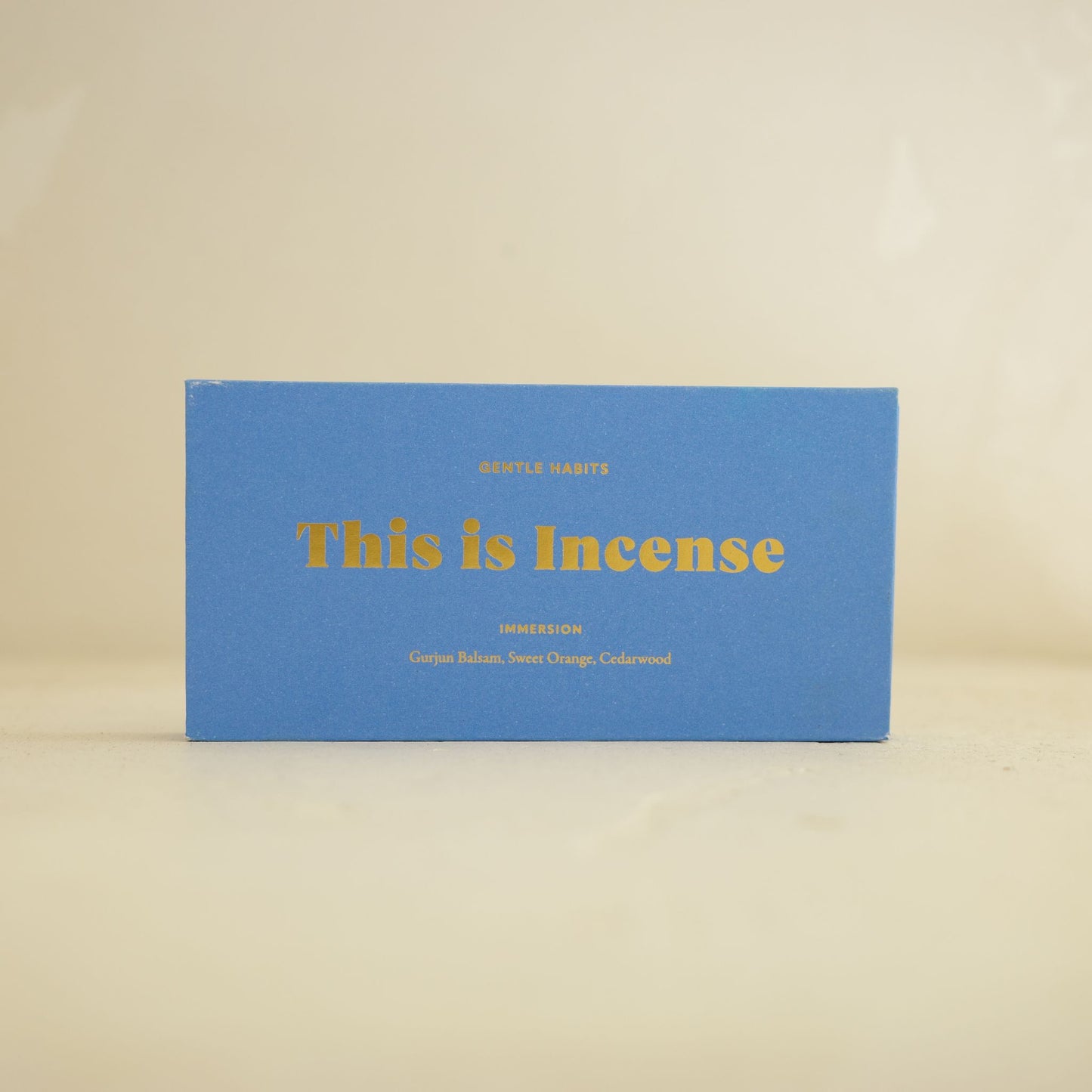 Front view of matte blue Gentle Habits incense box with gold typography on beige background by 9to5 Studios