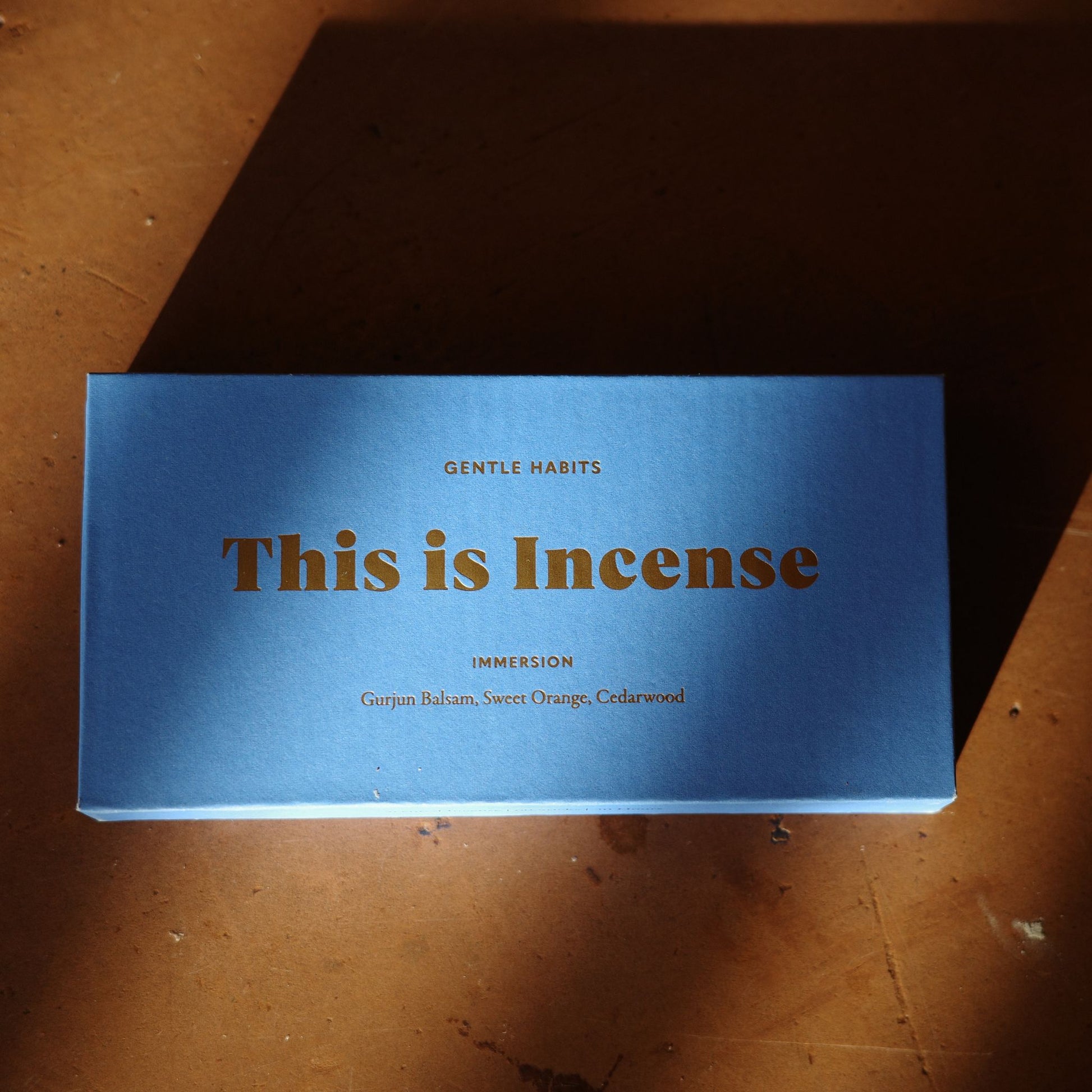 Blue textured cardboard incense box with gold text on rustic wooden surface by 9to5 Studios