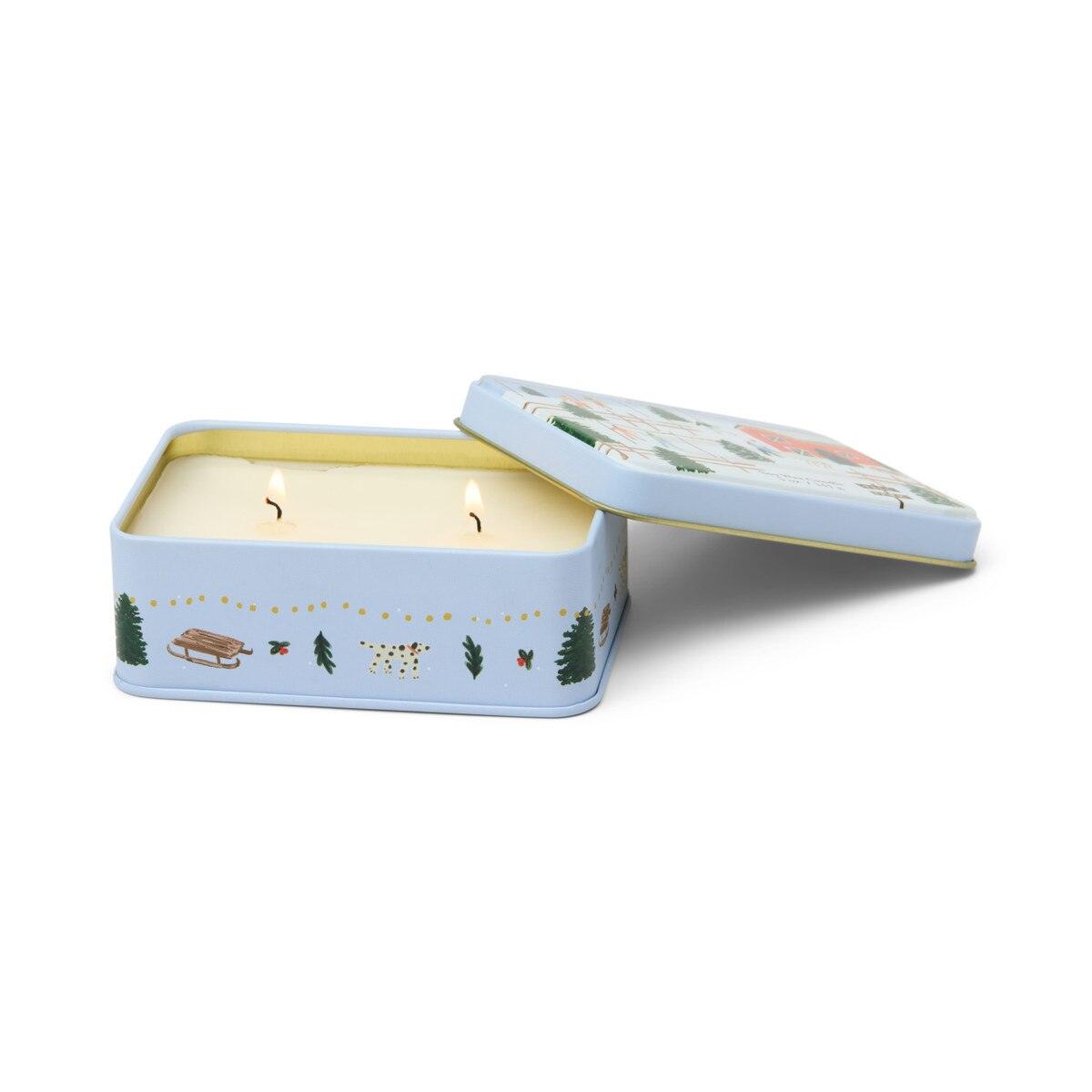 Paddywax Vanilla Bean two-wick soy candle in matte blue tin with open lid showing lit wicks and tree farm scene
